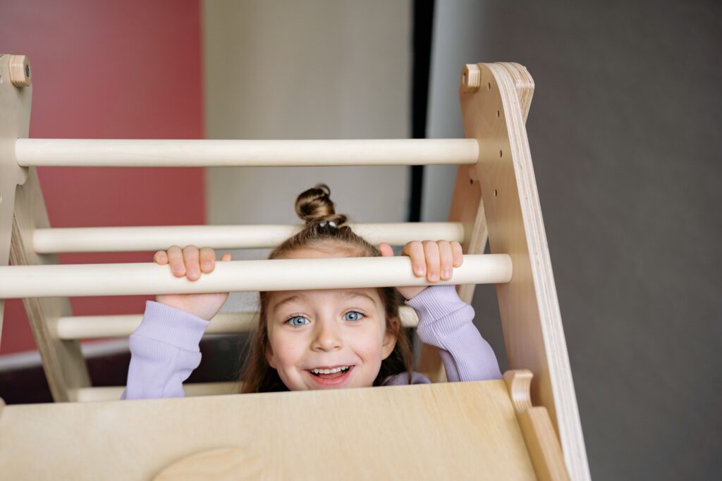 Joyful young girl playing on an indoor wooden climbing frame, smiling brightly.